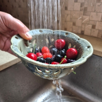 Handmade pottery berry bowl being used to rinse fresh cherries and berries under running water